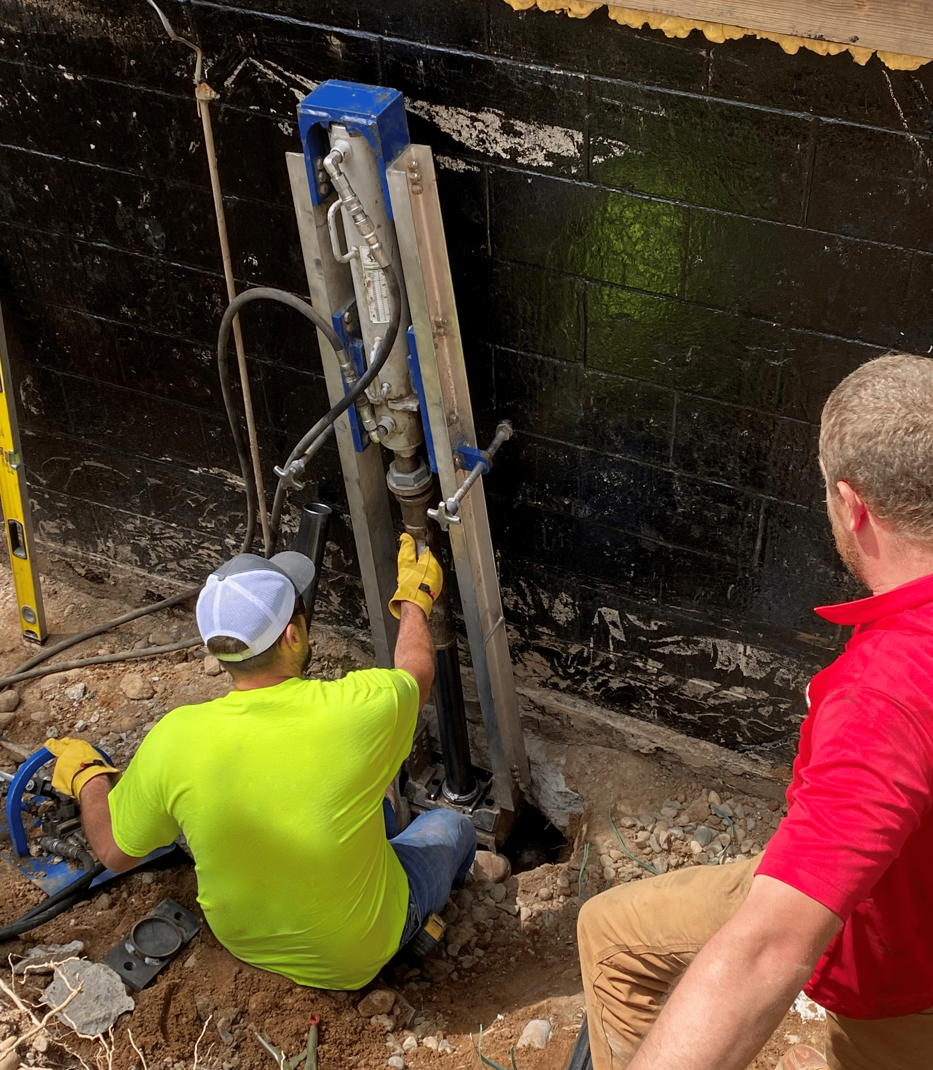 Foundation repair crew excavating soil around home exterior for foundation stabilization